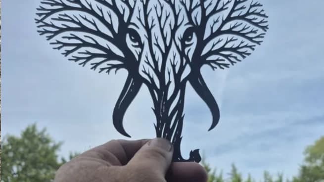 Árbol con forma de elefante recortado en metal, sostenido contra el cielo
